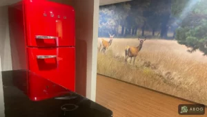 Naast een zwart aanrechtblad staat een rode koelkast. Op de muur in de gang ernaast is een fotobehang met herten in een open veld te zien.