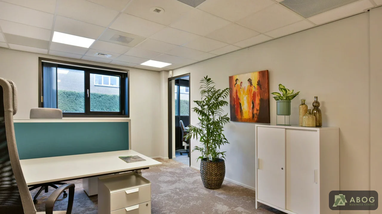 Een lichte kantoorruimte met een bureau, bureaustoel, ladeblok en een witte kast. Aan de muur hangt een kleurrijk schilderij en er staat een grote kamerplant.