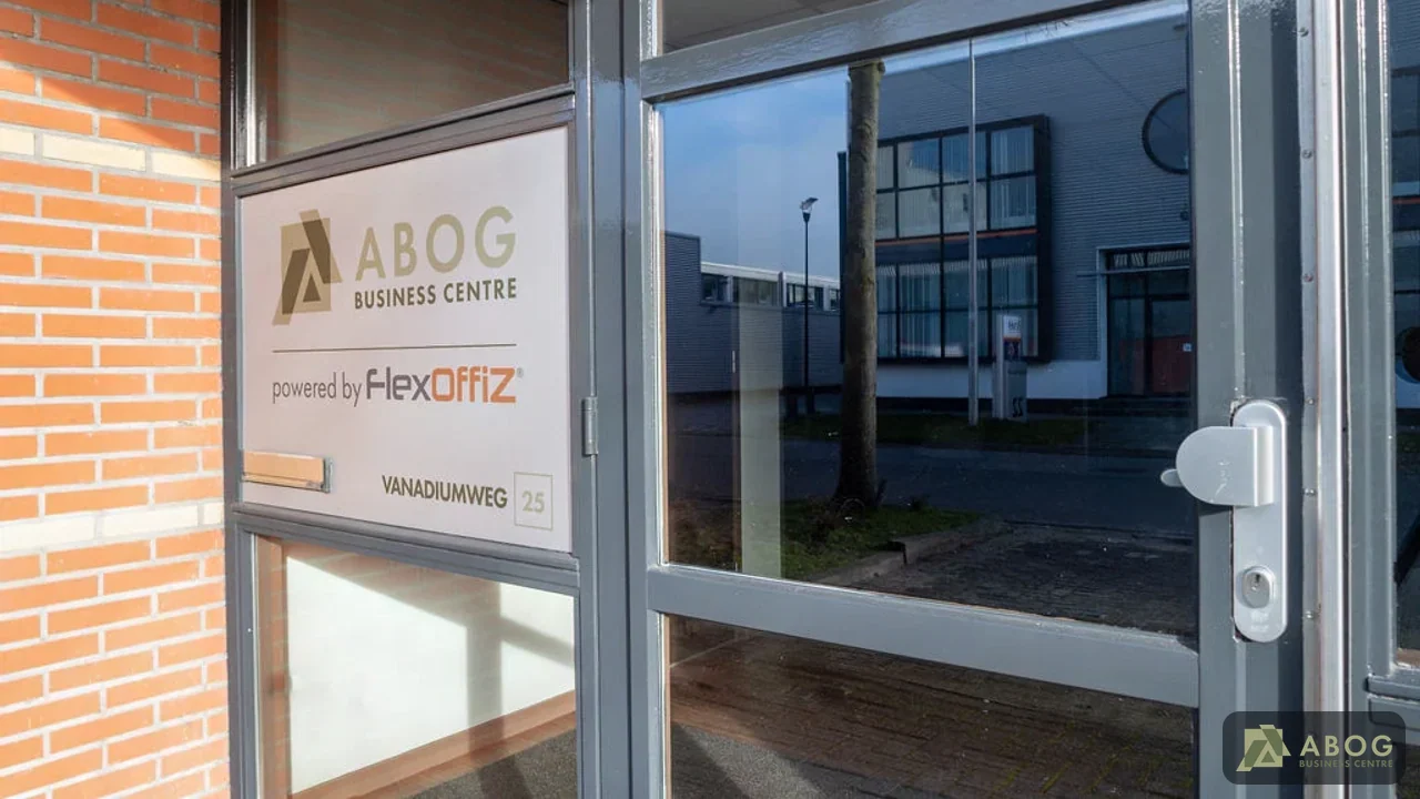 Een glazen toegangsdeur van een modern kantoorgebouw met grijze kozijnen en een informatiebord. In de ruit weerspiegelt de overkant van de straat bij daglicht.